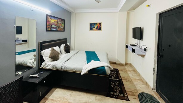 A hotel room with a bed, a ceiling fan, a TV, and artwork on the walls. - Roomshala Hotel South Embassy (New Delhi)