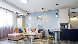 A modern living room with a sofa, coffee table, and dining table. There is a kitchen area with cabinets and a microwave. - Apartment by Luxe Group SN400 (Yerevan)