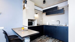 A compact kitchen with a wooden floor, a dining table with chairs, a hanging light fixture, and built-in appliances. - Apartment by Luxe Group SN400 (Yerevan)