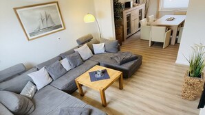 A modern living room with a large grey sectional sofa, a wooden coffee table, and a dining area with a wooden table and chairs.