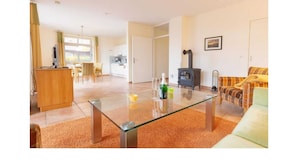 A spacious living room with a glass coffee table, a sofa, a fireplace, and a kitchen in the background. - Suurhusen - Greetsiel (Greetsiel)