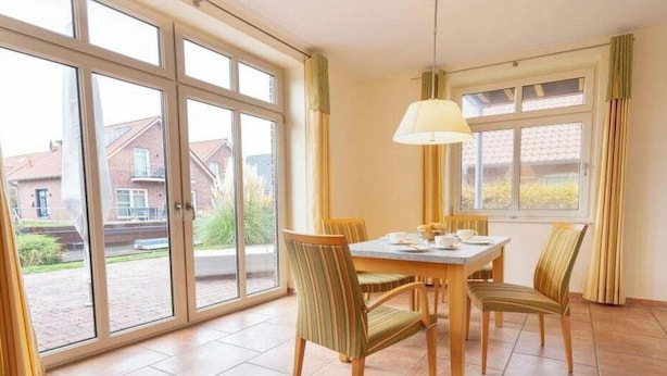 A dining area with a table set for four, surrounded by chairs, a hanging lamp, and large windows offering a view of the outside. - Suurhusen - Greetsiel (Greetsiel)