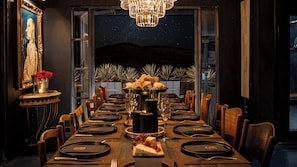 A formal dining room with a long table set for a meal, a chandelier, and a view of the night sky. - Iconic 6BR Desert Retreat w/ Pool, Pickleball & Fire Pit Joshua Tree Mansion by Avantstay (Joshua Tree)