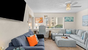 A living room with a gray sofa, ottoman, and a gray sectional sofa. There is a desk with a lamp and a painting on the wall. - Steps From the Sand Bright Coastal Stay w/ Pool Access Coastal Hideaway by Avantstay (Destin)