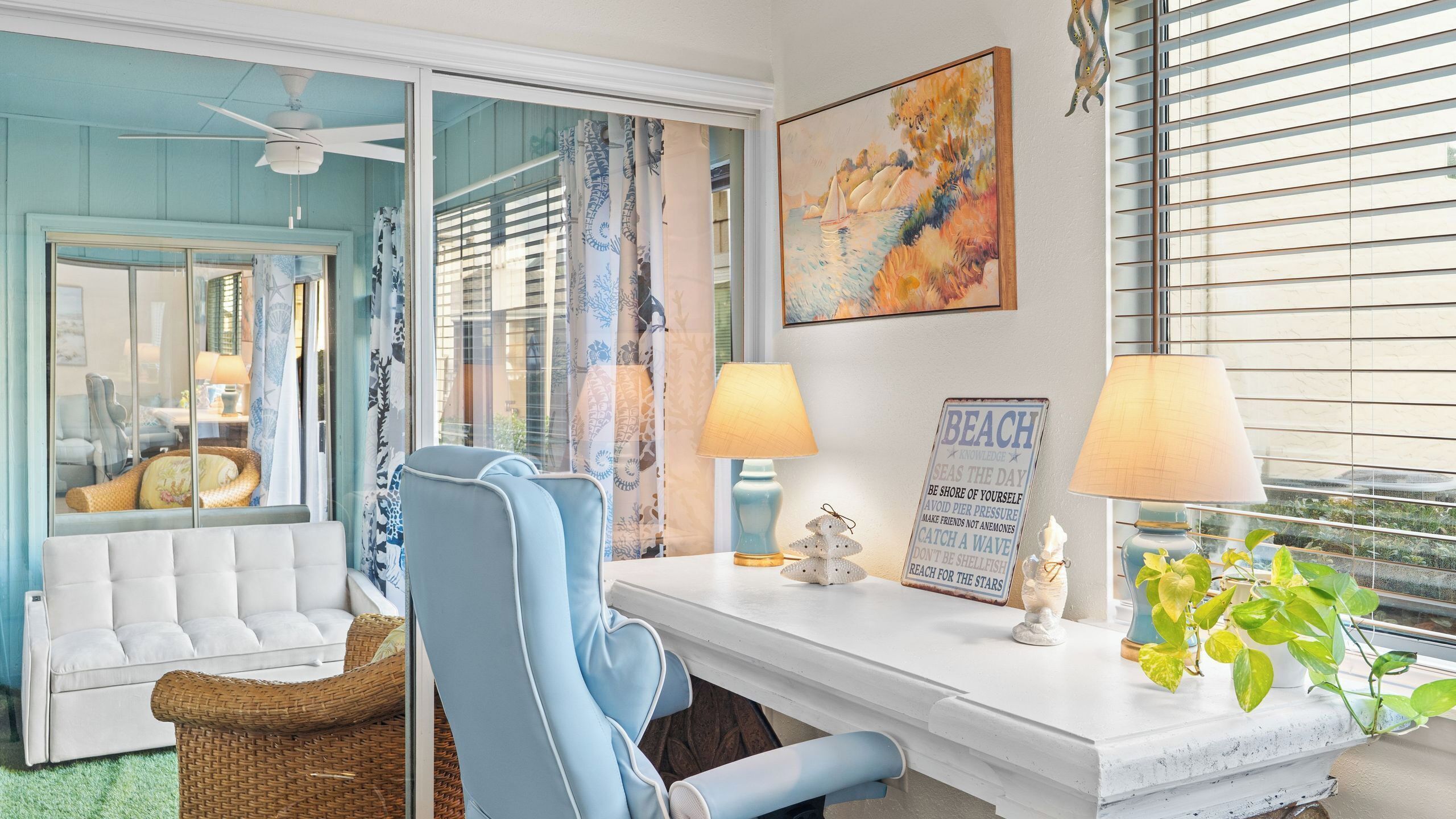 Une pièce avec un canapé blanc, une chaise bleue, une table blanche avec deux lampes, un panneau décoratif et une plante.
