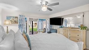 Quarto com cama, cômoda, televisão e vista para o exterior.
