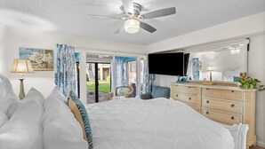 A bedroom with a bed, dresser, TV, and a view of the outdoors. - Steps From the Sand Bright Coastal Stay w/ Pool Access Coastal Hideaway by Avantstay (Destin)