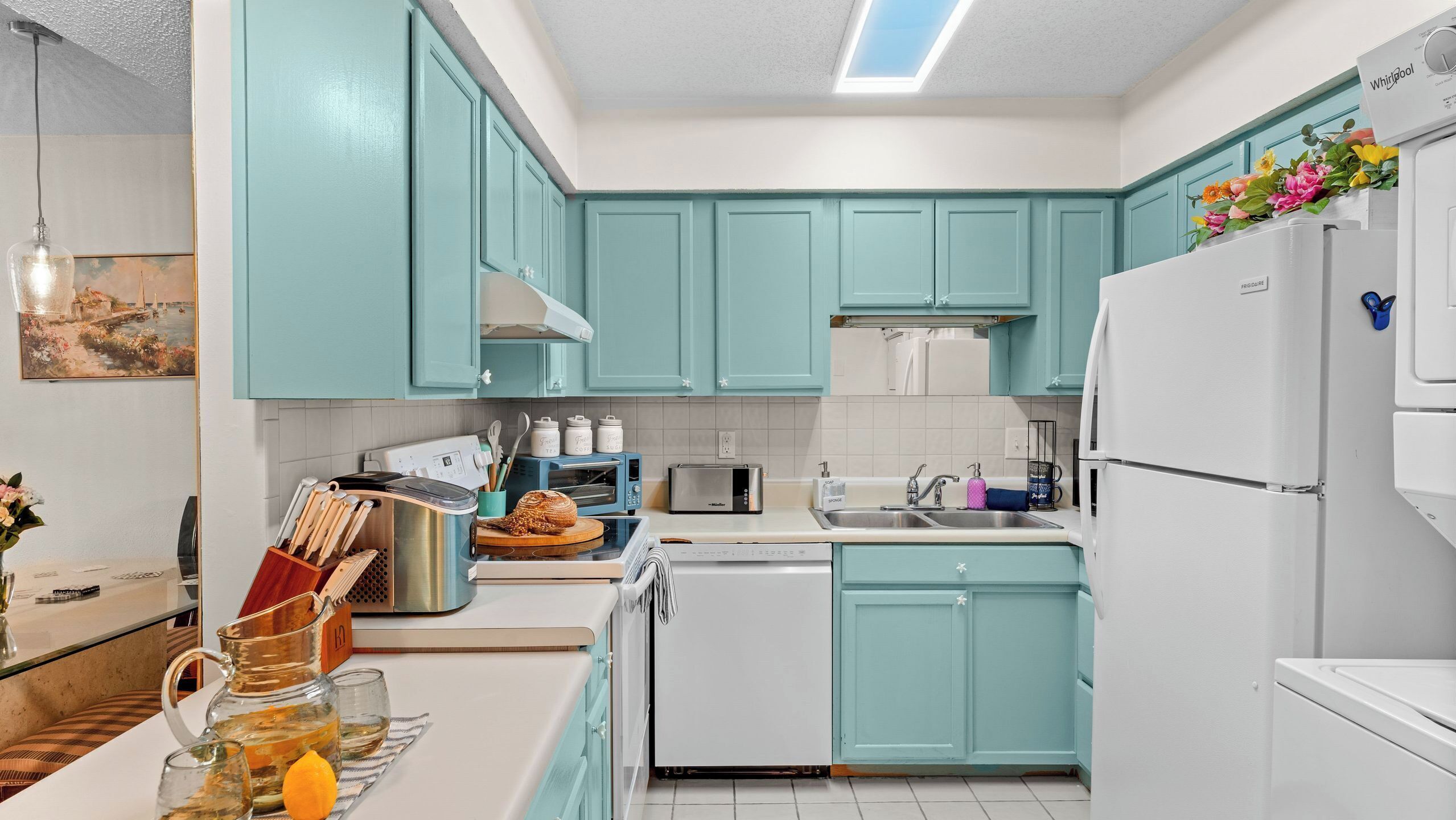 A kitchen with teal cabinets, a white refrigerator, a toaster, and a sink.