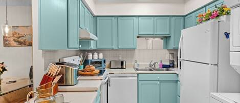 A kitchen with teal cabinets, a white refrigerator, a toaster, and a sink.