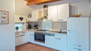 A modern kitchen with white cabinets, a stainless steel range hood, a built-in oven, and a coffee maker. - Holiday home with 3 bedrooms (Greetsiel)