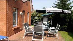 An outdoor patio with a brick wall, a table with four chairs, and a white umbrella. - Holiday home with 3 bedrooms (Greetsiel)