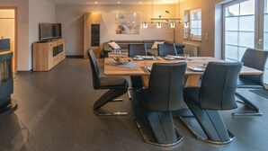 Een moderne eetruimte met een lange tafel, zwarte stoelen en een televisie op een houten kast.
