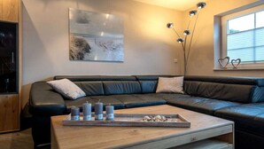 Een moderne woonkamer met een zwarte leren bank, een houten salontafel met kaarsen, en een schilderij aan de muur.