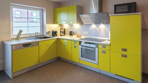 Een kleine keuken met gele kastjes, een roestvrijstalen afzuigkap, een magnetron en een vaatwasser.