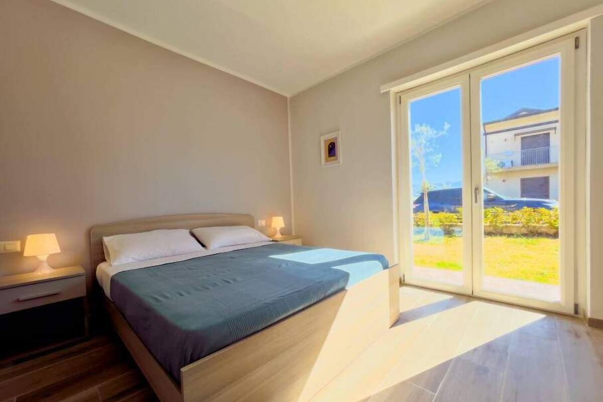 Une chambre à coucher comprenant un lit, des tables de chevet, une fenêtre donnant sur l’extérieur et une porte menant à un balcon.