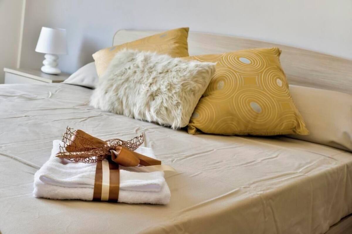 Un lit bien fait, agrémenté d’une pile de serviettes blanches et brunes, d’un oreiller blanc moelleux et d’un oreiller jaune à motifs.
