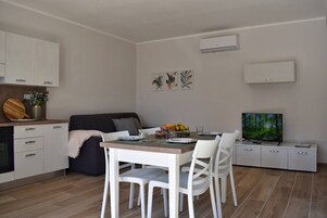 Una cocina moderna con armarios blancos, una mesa de comedor con sillas, un sofá y un televisor sobre un mueble blanco.