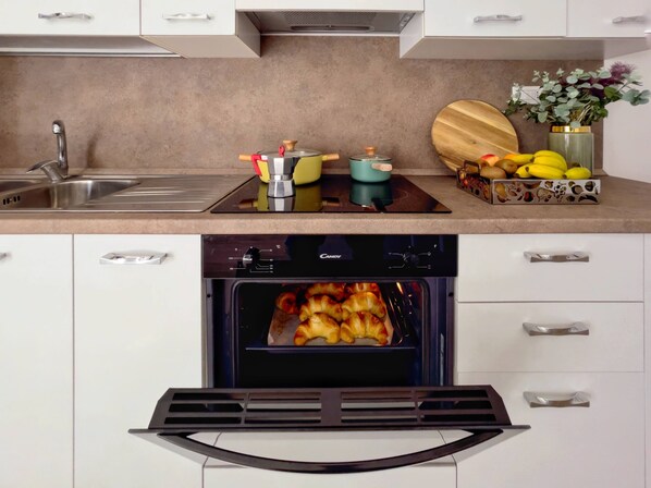 Una cocina moderna con horno empotrado, un lavamanos y una encimera con tabla de cortar y frutas.