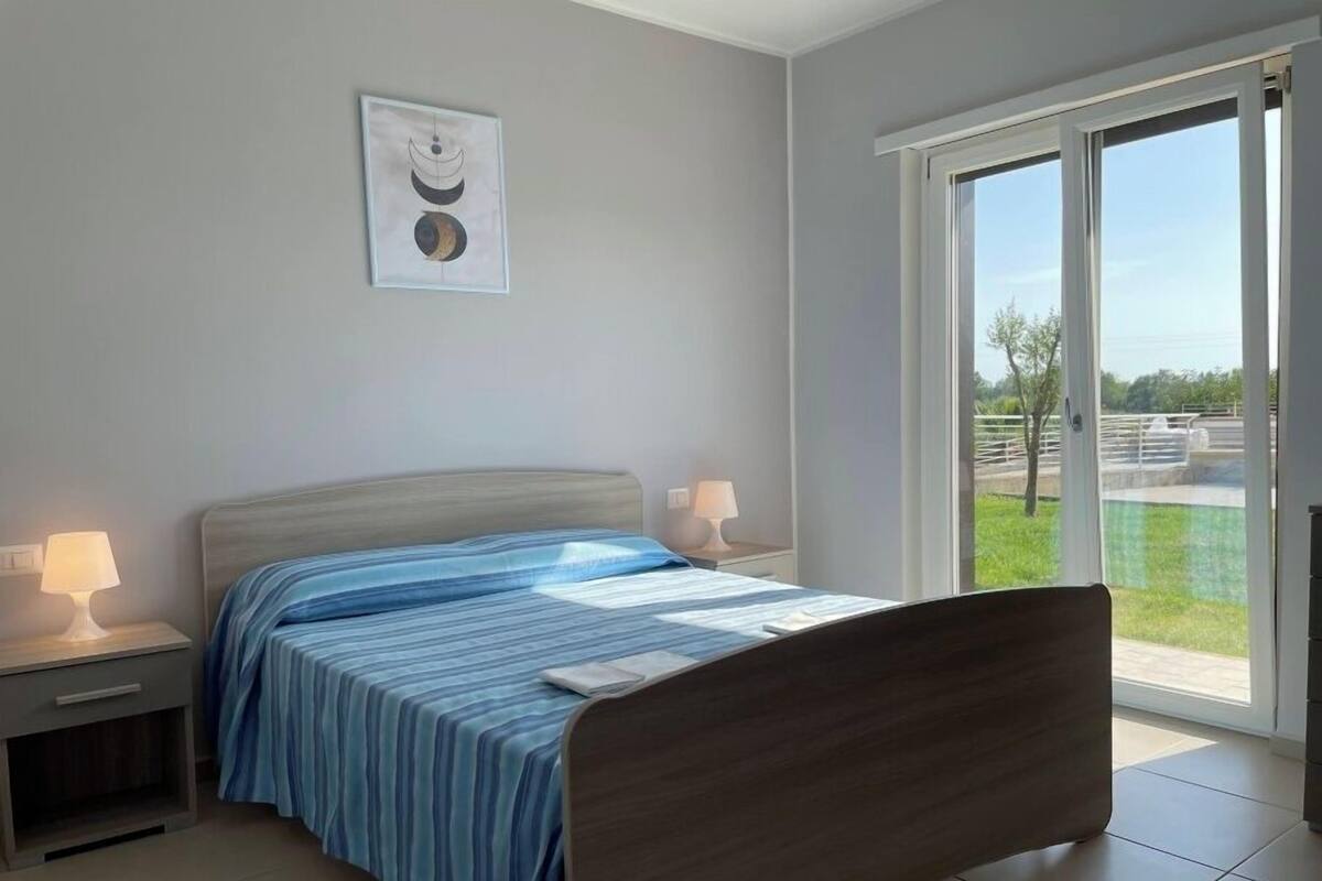 Une chambre à coucher avec un lit, des tables de chevet, une fenêtre donnant sur un paysage agréable et un tableau accroché au mur.