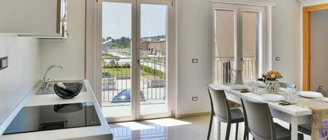 A modern kitchen with a built-in dishwasher, a large window with a view of a parking area, and a dining area with a table set for two.