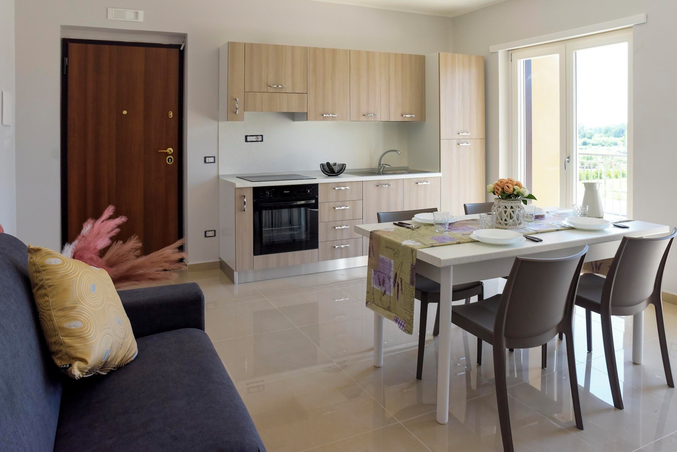 A modern kitchen with light wood cabinets, a built-in oven, and a dining area with a table set for two.