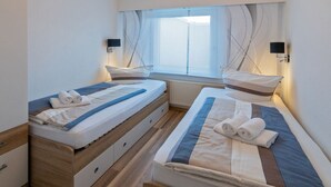 Ein Schlafzimmer mit zwei Betten, Holzböden, einem Fenster mit Vorhängen und Nachttischlampen.