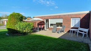 Ein Backsteinhaus mit einer Terrasse, ausgestattet mit Tisch, Stühlen und einer Bank.