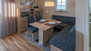 Ein kompakter Wohnraum mit Esstisch, zwei Stühlen, einer Couch, einem Schrank mit Glastüren und einem Fenster mit Blick.