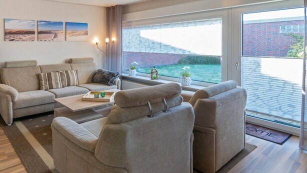 Ein modernes Wohnzimmer mit einer Sofagarnitur, einem Couchtisch und Blick auf ein Ziegelgebäude durch große Fenster.