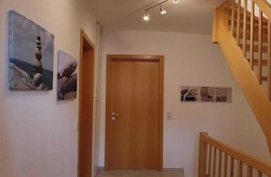 A hallway with a wooden door, a staircase, and wall-mounted pictures.