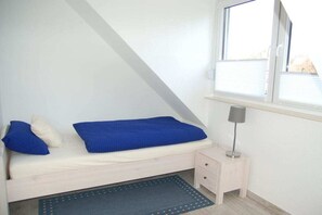 Une petite chambre avec un lit simple, une table de chevet, une lampe et une fenêtre.
