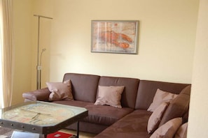 Un salon avec un canapé marron, des coussins à rayures, une table basse en verre avec une horloge, et un tableau encadré accroché au mur.