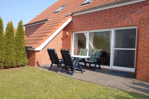 Une maison en briques avec un patio, deux chaises, une table et une porte-fenêtre coulissante.