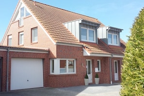A two-story house with a red brick exterior, a white garage door, and a small front porch with a potted plant.