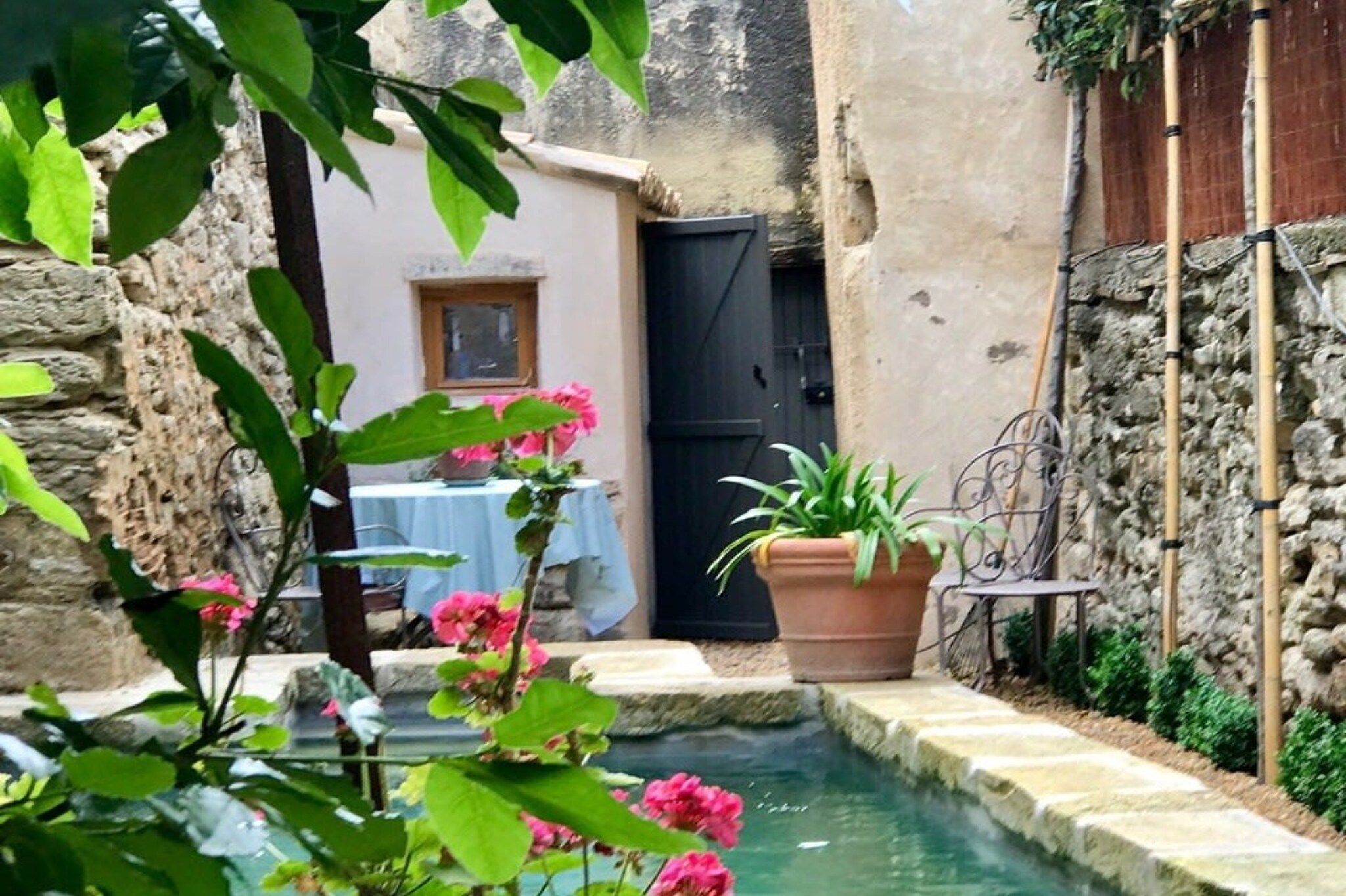 A narrow courtyard with a water feature, a table with a blue tablecloth, and potted plants.