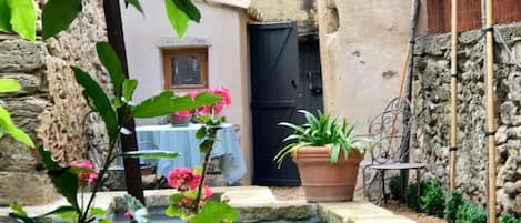 A narrow courtyard with a water feature, a table with a blue tablecloth, and potted plants.