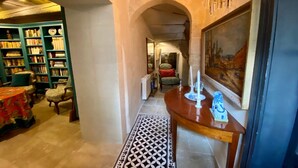 A hallway with a wooden ceiling, a green bookshelf, a dining table with a vase, and a painting on the wall. - Heated Pool Apartment in Uzes (Uzès)