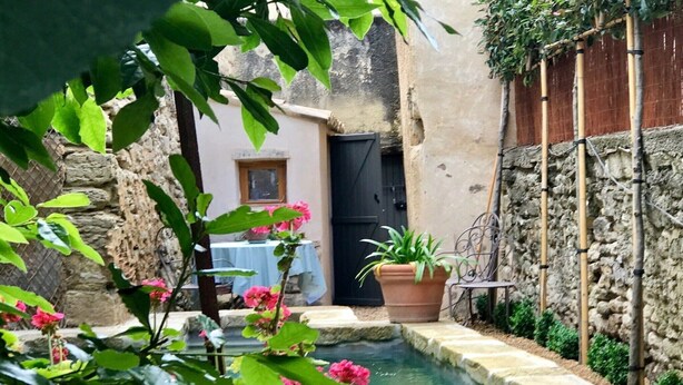 A small courtyard with a pool, stone walls, a table with a chair, and potted plants. - Heated Pool Apartment in Uzes (Uzès)
