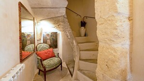 A narrow stairway with a stone wall, a chair with a red cushion, and a mirror reflecting a painting. - Heated Pool Apartment in Uzes (Uzès)