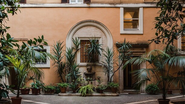 Ein Innenhof mit Kopfsteinpflasterboden, umgeben von Blumentöpfen und einem Gebäude mit warmer Fassade.