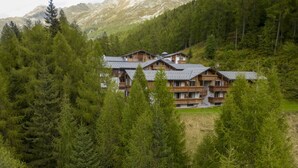 A wooden lodge with multiple balconies, surrounded by dense forest and mountains.