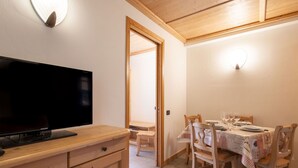 A dining area with a table set for six, wooden chairs, and a television on a wooden cabinet.