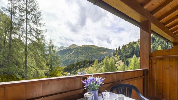A wooden deck with a table set for two, overlooking a mountainous landscape.
