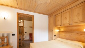 A bedroom with a wooden headboard, a bed, a wooden bench, a chair, and a radiator.