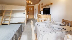 A room with bunk beds, a desk with a computer, and a dining table set for four.