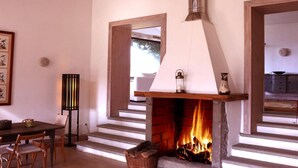A fireplace with logs, a dining table with chairs, and a framed picture on the wall.