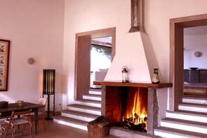 A fireplace with logs, a dining table with chairs, and a framed picture on the wall.