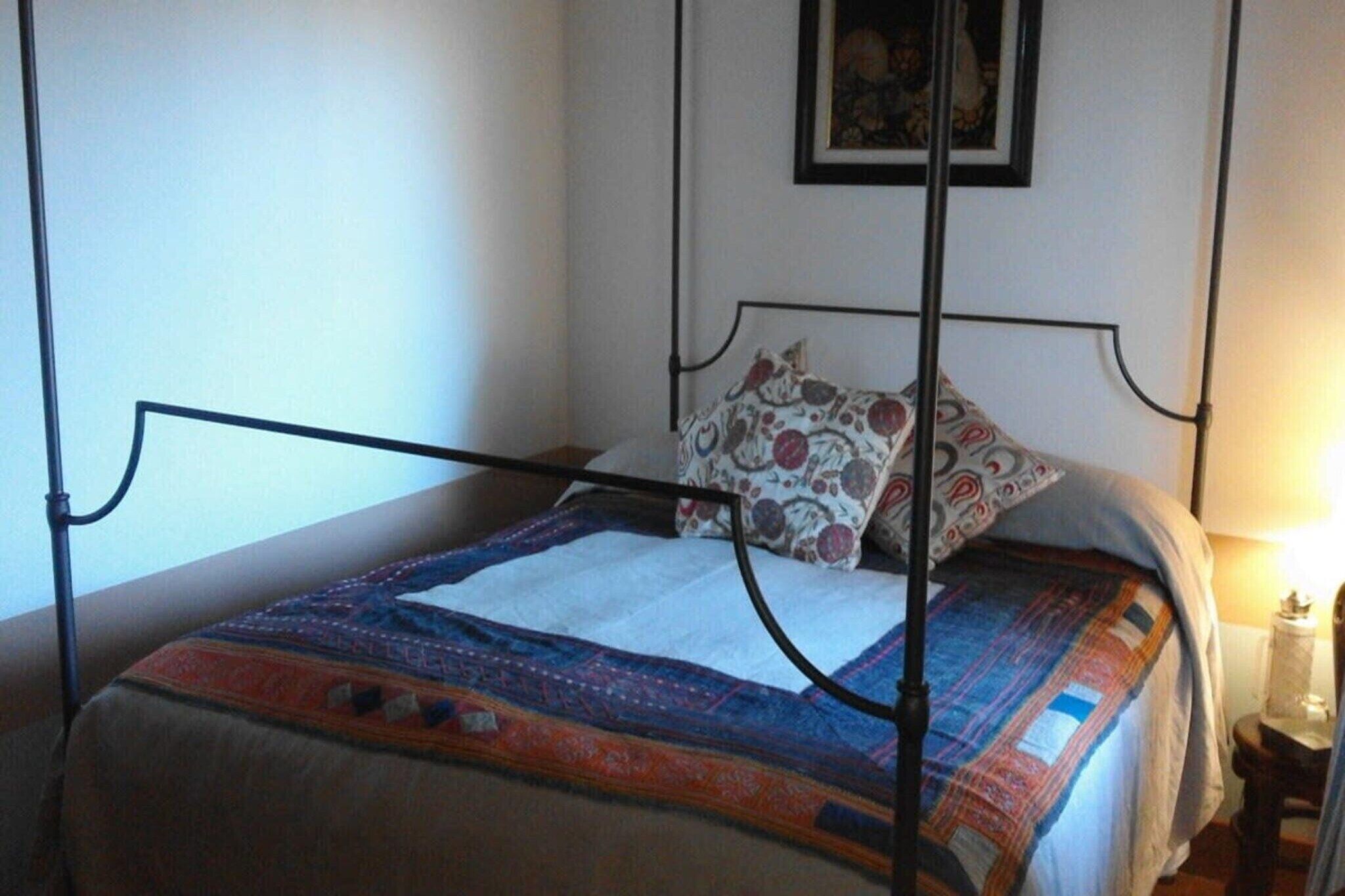 A single bed with a metal frame, a patterned bedspread, and a pillow with a floral design.