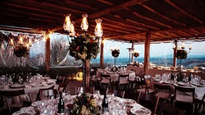 An outdoor dining area with tables set for a meal, surrounded by wooden beams and string lights.
