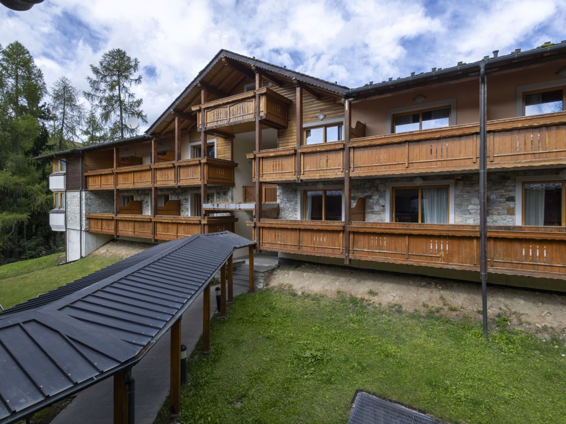A multi-story wooden building with balconies, stone walls, and a grassy yard.